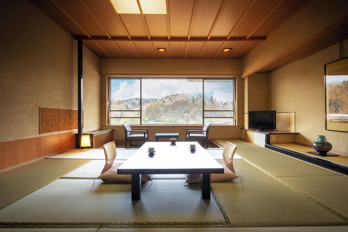 Une pièce traditionnelle avec tatamis, comprenant une table basse, des nattes de tatami et un téléviseur posé sur un meuble.