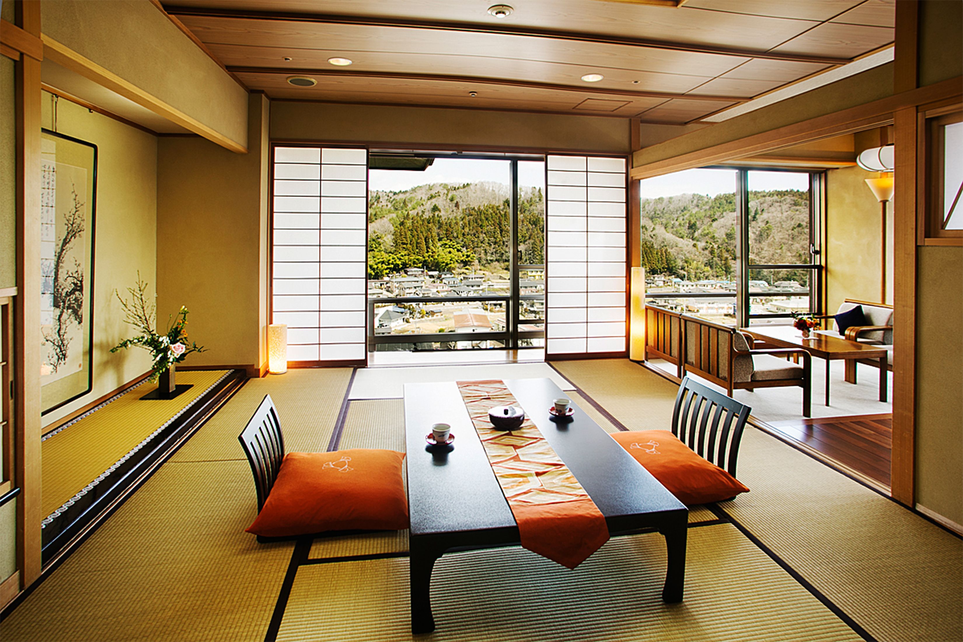 Ein traditioneller japanischer Raum mit Tatami-Böden, einem niedrigen Tisch mit Kissen und Blick auf eine Berglandschaft durch große Schiebetüren.