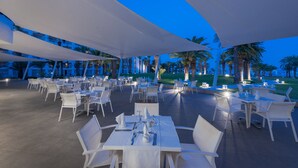 An outdoor dining area with white tables and chairs, shaded by large white canopies, and palm trees in the background. - Hotel Tour Khalef (Sousse)