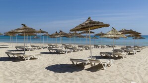 A beach with rows of white lounge chairs and thatched umbrellas. - Hotel Tour Khalef (Sousse)