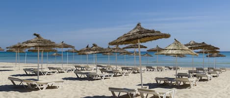 Een privéstrand, wit zand, ligstoelen aan het strand, parasols