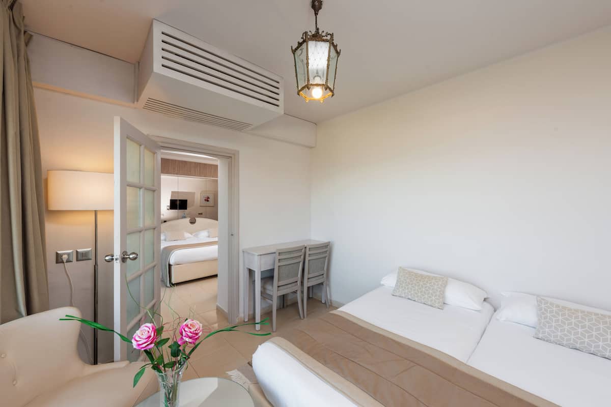 Quarto de hotel com uma cama, uma escrivaninha, uma cadeira, um abajur e um vaso com flores.