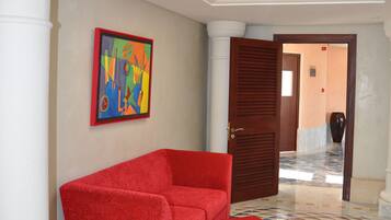 Un sofá rojo y un reposapiés en un pasillo con un estampado geométrico colorido en el suelo y una lámpara en el techo.