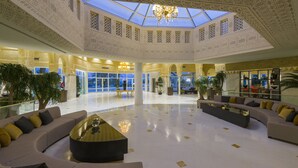 A spacious lobby with a high ceiling, intricate ceiling patterns, and a central seating area with sofas and a coffee table. - Hotel Tour Khalef (Sousse)