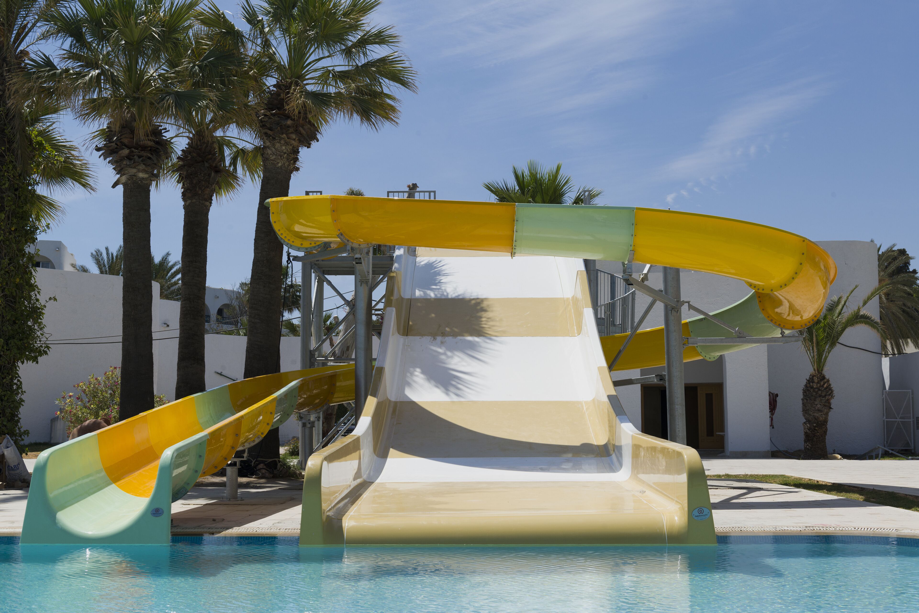 Ein Pool mit zwei Wasserrutschen, Palmen und blauem Himmel.