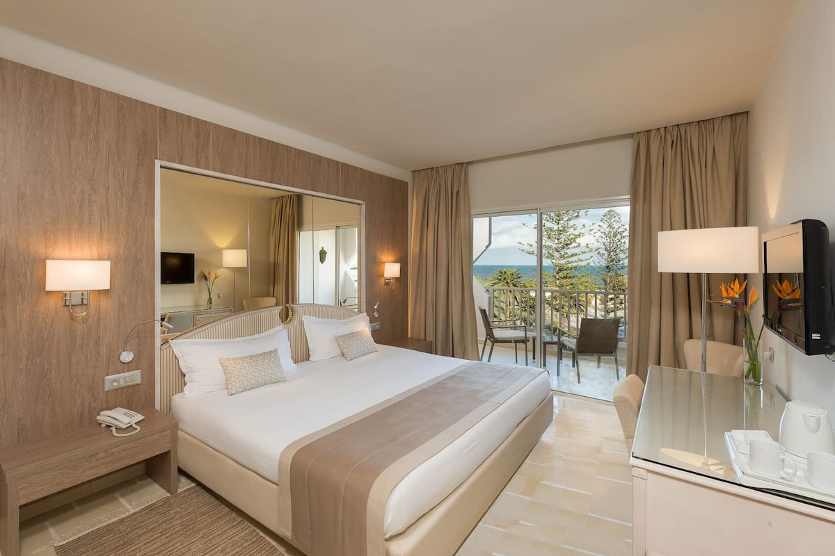 Quarto de hotel com uma cama grande, uma escrivaninha com cadeira, televisão e varanda com vista.