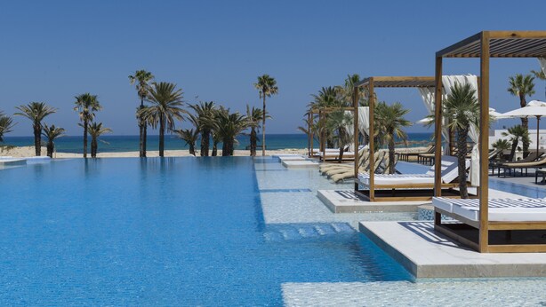 A clear blue pool with lounge chairs and umbrellas, surrounded by palm trees and a view of the beach. - Hotel Tour Khalef (Sousse)
