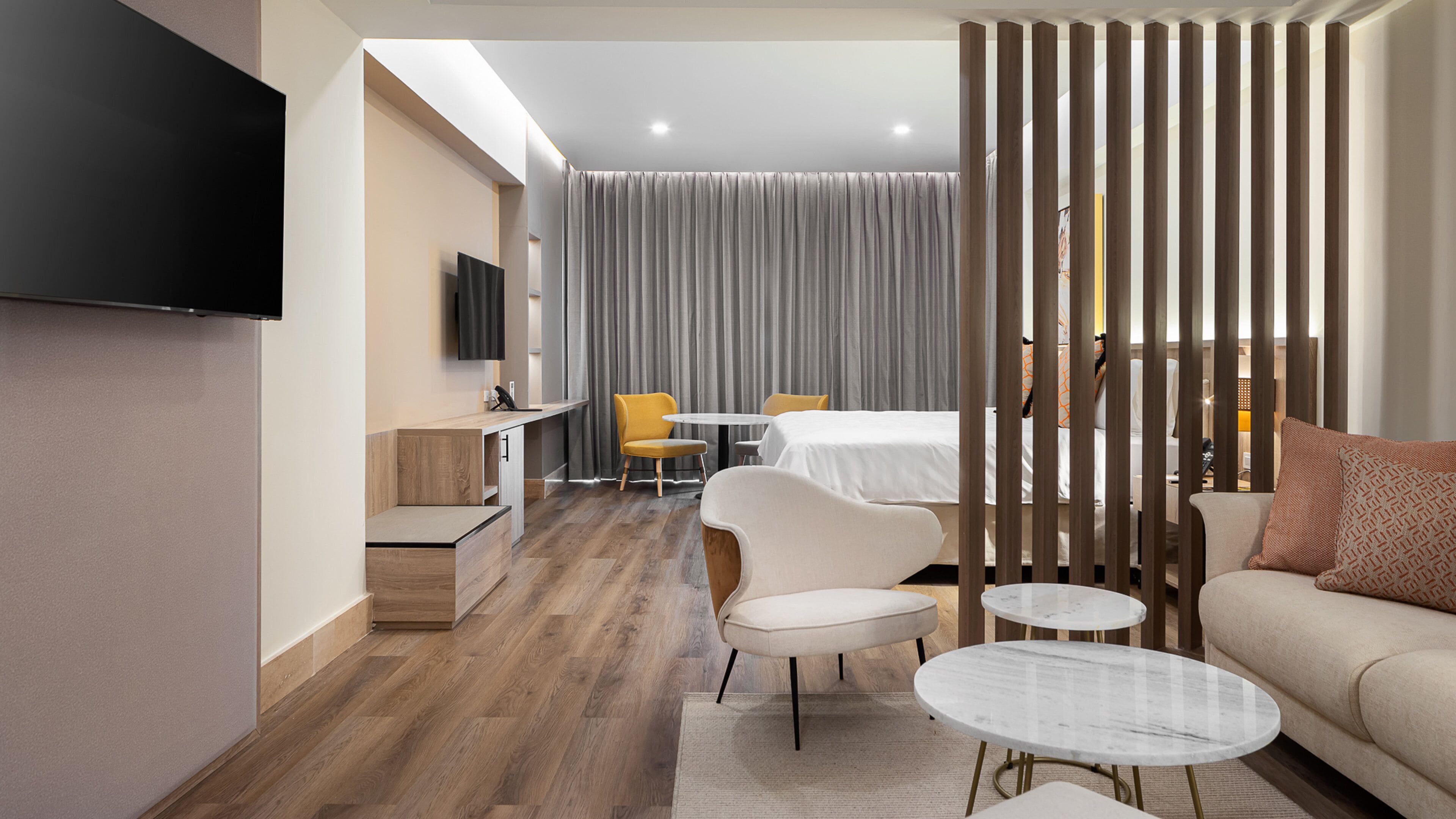 A modern hotel room with a flat-screen TV, a sofa, a dining table, and a bed.