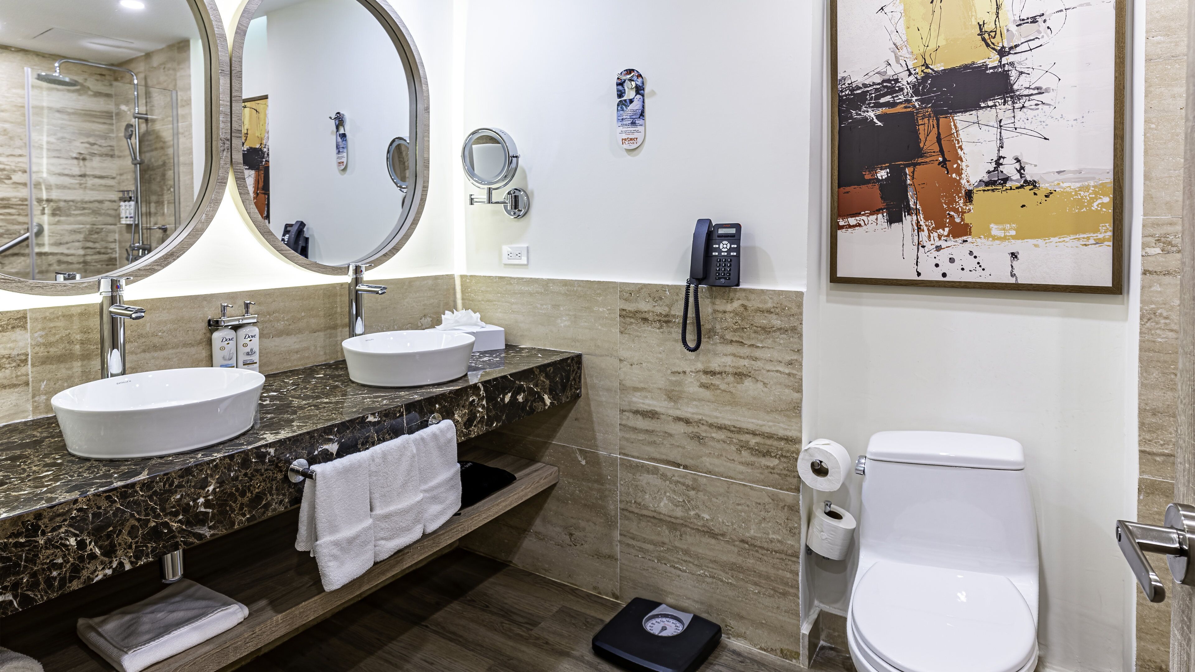 A modern bathroom with a large oval sink, a round mirror, a handheld showerhead, a toilet, and a scale.
