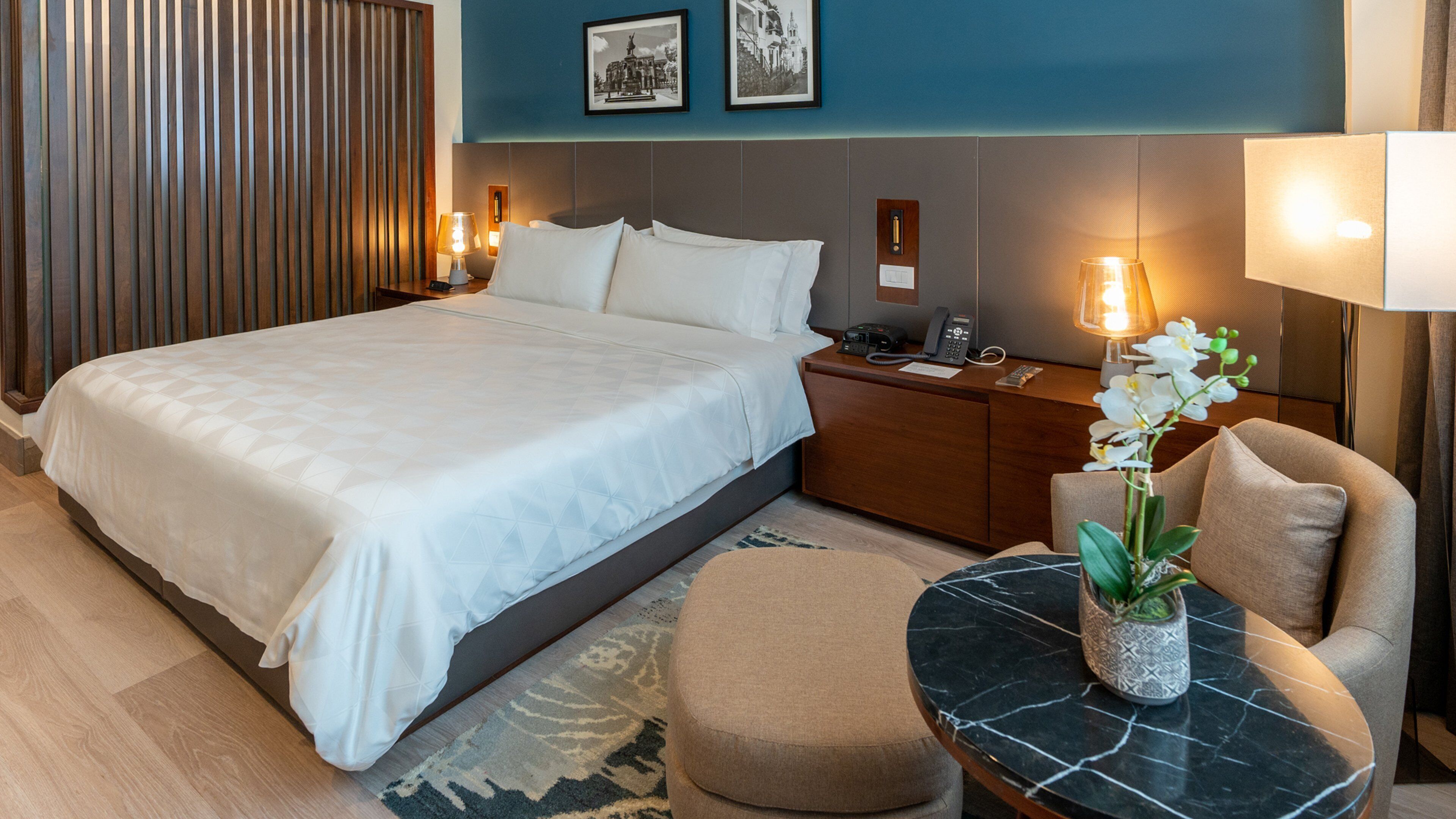 Ein Hotelzimmer mit einem großen Bett, einem Schreibtisch mit Lampe, einem Sessel und einem kleinen Tisch mit Blumen.