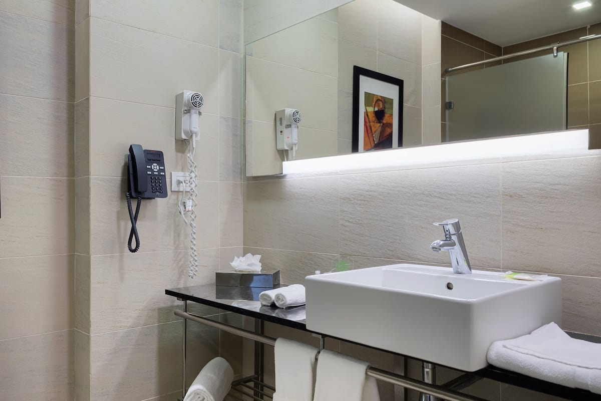 A modern bathroom with a glass sink, a white toilet, and a hairdryer mounted on the wall.