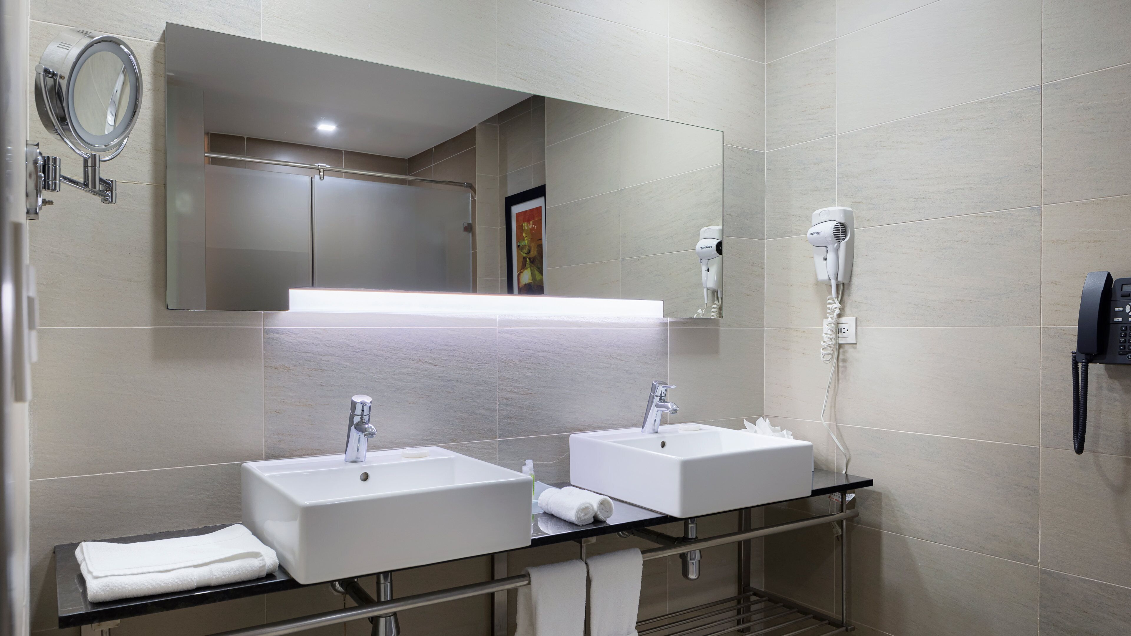 A modern bathroom with two sinks, a mirror, a hairdryer, and a phone.