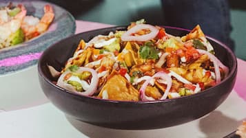 Un tazón de nachos cubiertos de queso, cebollas y jalapeños.