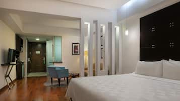 Een moderne hotelkamer met een groot bed, een bureau met een stoel, een televisie en een badkamer zichtbaar door een glazen deur.