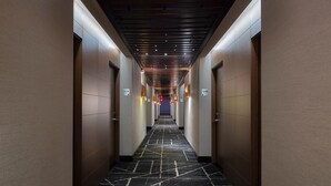 Un couloir d’hôtel moderne avec un sol en marbre, des portes en bois et un éclairage encastré.