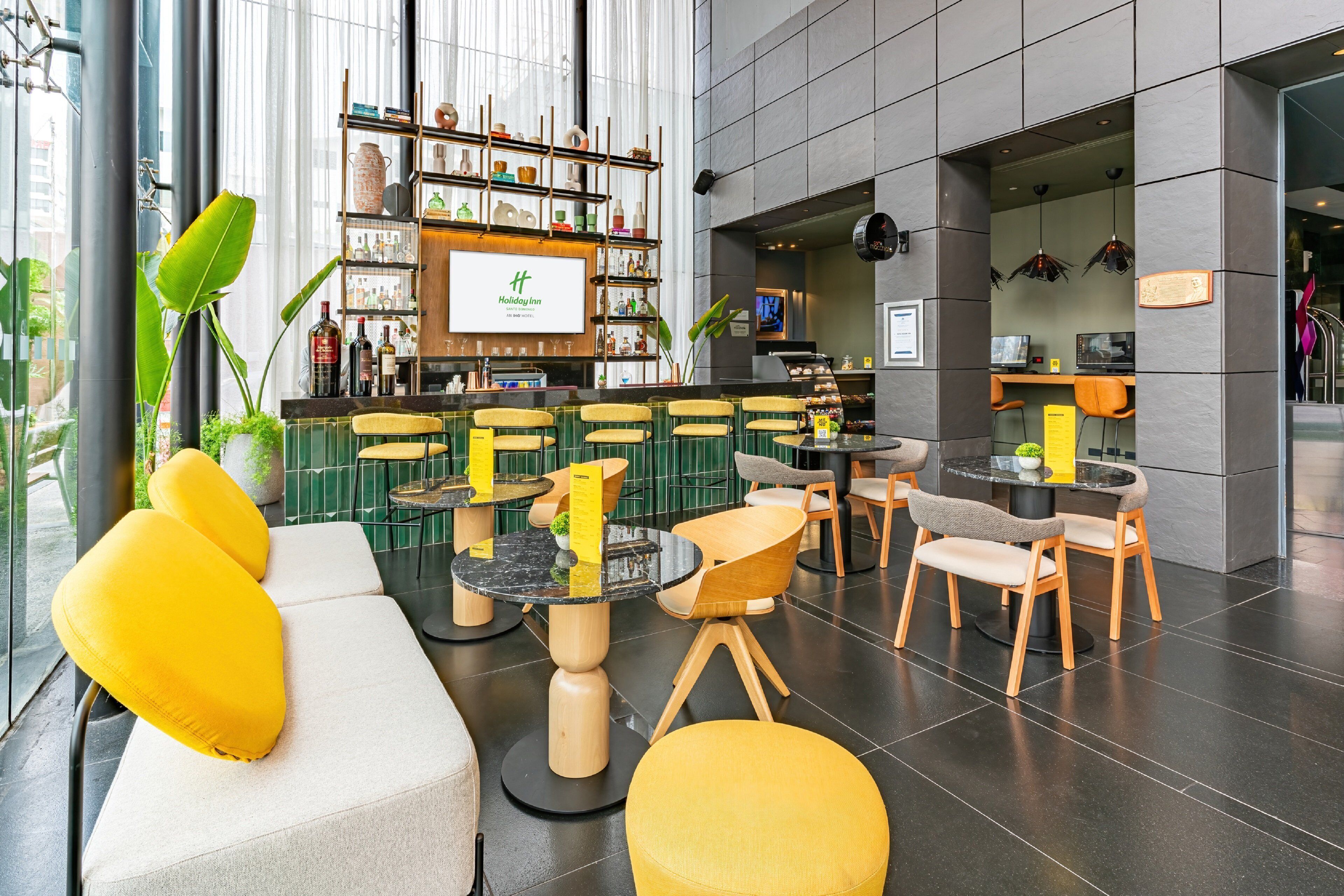 A modern hotel lobby with a bar area, seating arrangements, and a large window providing natural light.