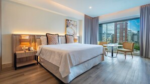 Une chambre d’hôtel moderne avec un grand lit, une table de chevet avec une lampe et une vue sur la ville grâce à de grandes fenêtres.