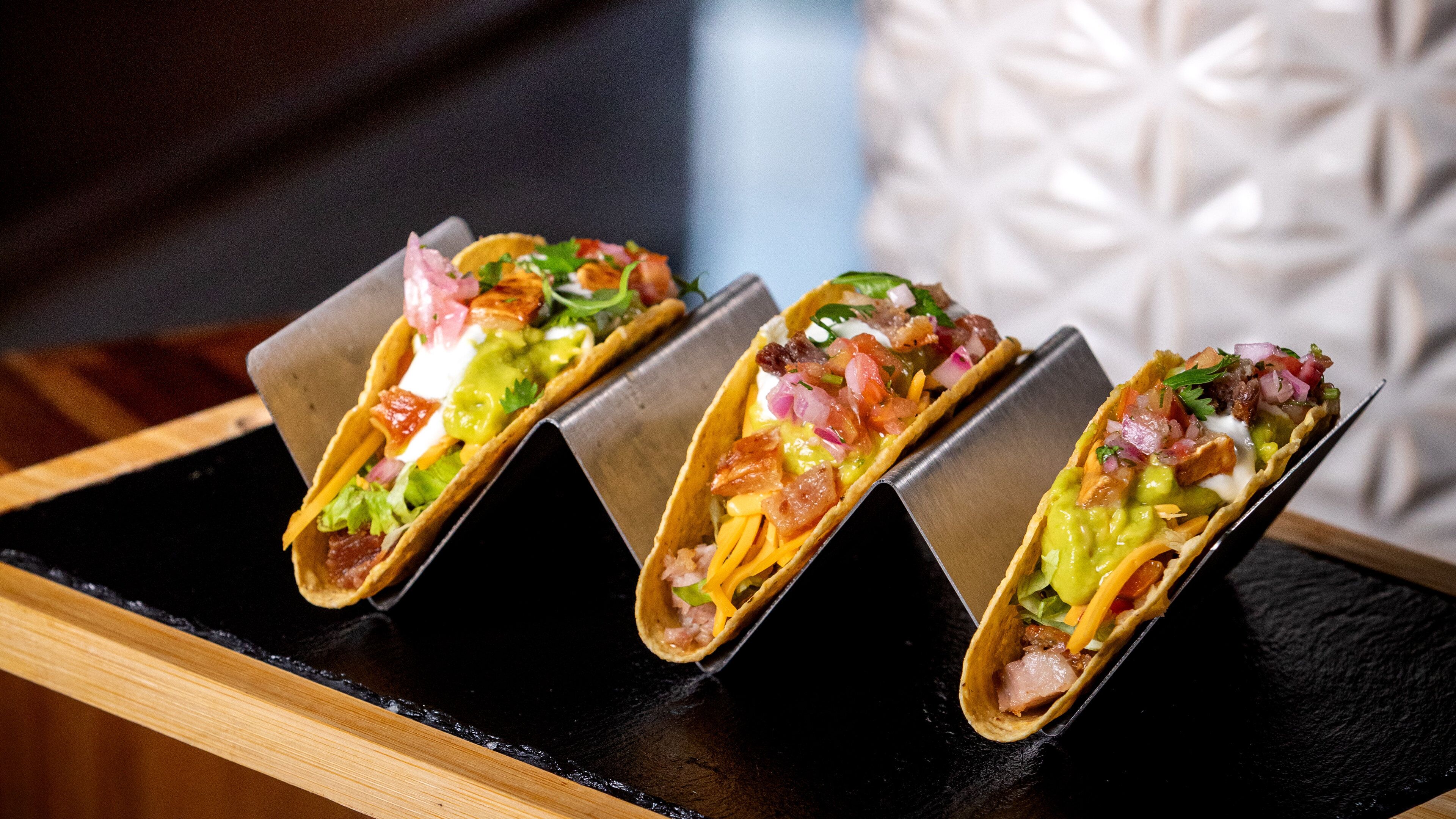 Tres tacos sobre una bandeja negra.