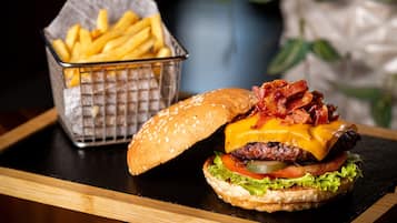 A burger with bacon, cheese, and lettuce on a bun, accompanied by a basket of fries.