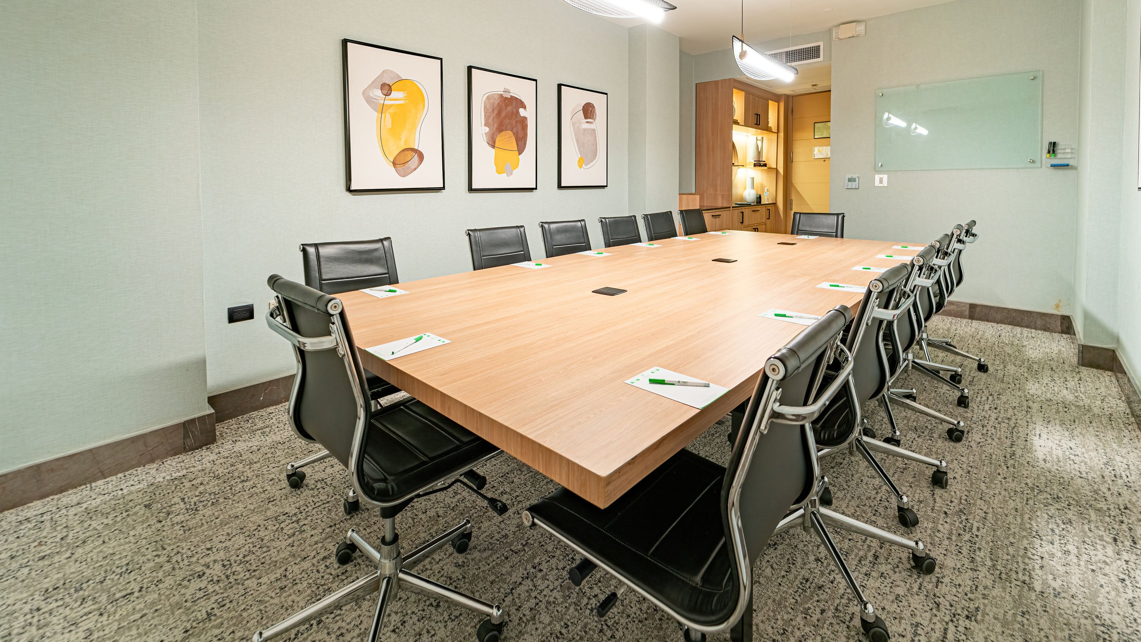 A conference room with a long table, black chairs, and framed artwork on the wall.