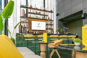 A Holiday Inn lobby with a bar area, seating, and a large screen displaying the hotel name.