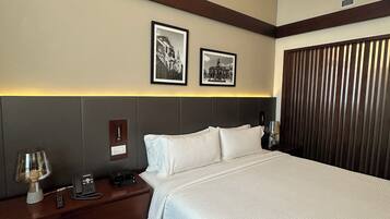 Una habitación de hotel con una cama grande, una mesita de noche con lámpara, un teléfono y dos cuadros en la pared.