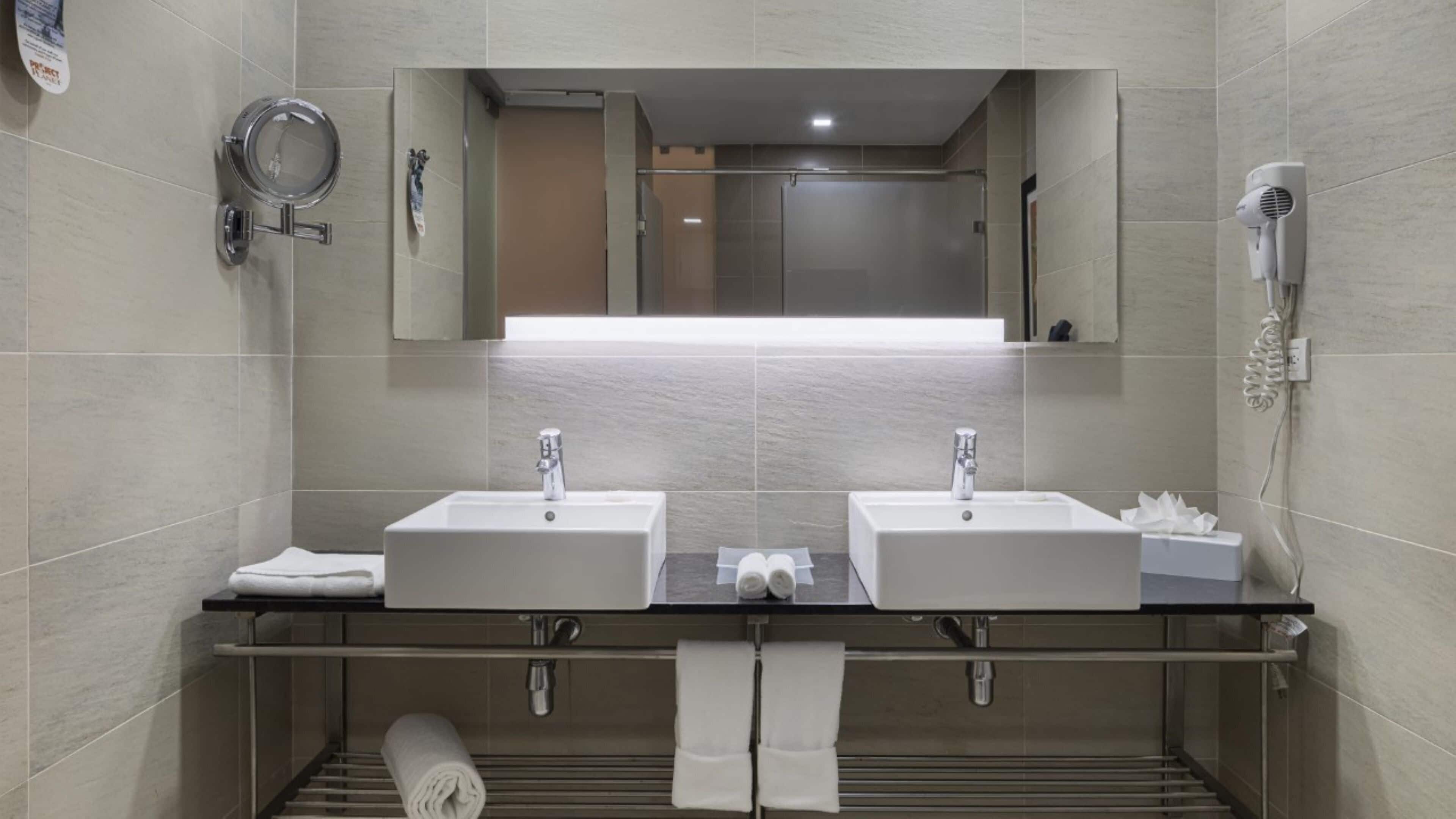 A modern bathroom with two sinks, a large mirror, a towel rack, and a hairdryer.