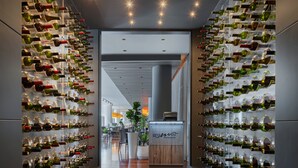 Une cave à vin avec des bouteilles rangées sur des étagères, un comptoir d’accueil en bois et, au fond, un espace dédié à la restauration.