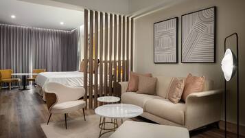 Quarto de hotel moderno com sofá, poltronas, mesa de jantar e um espelho grande.