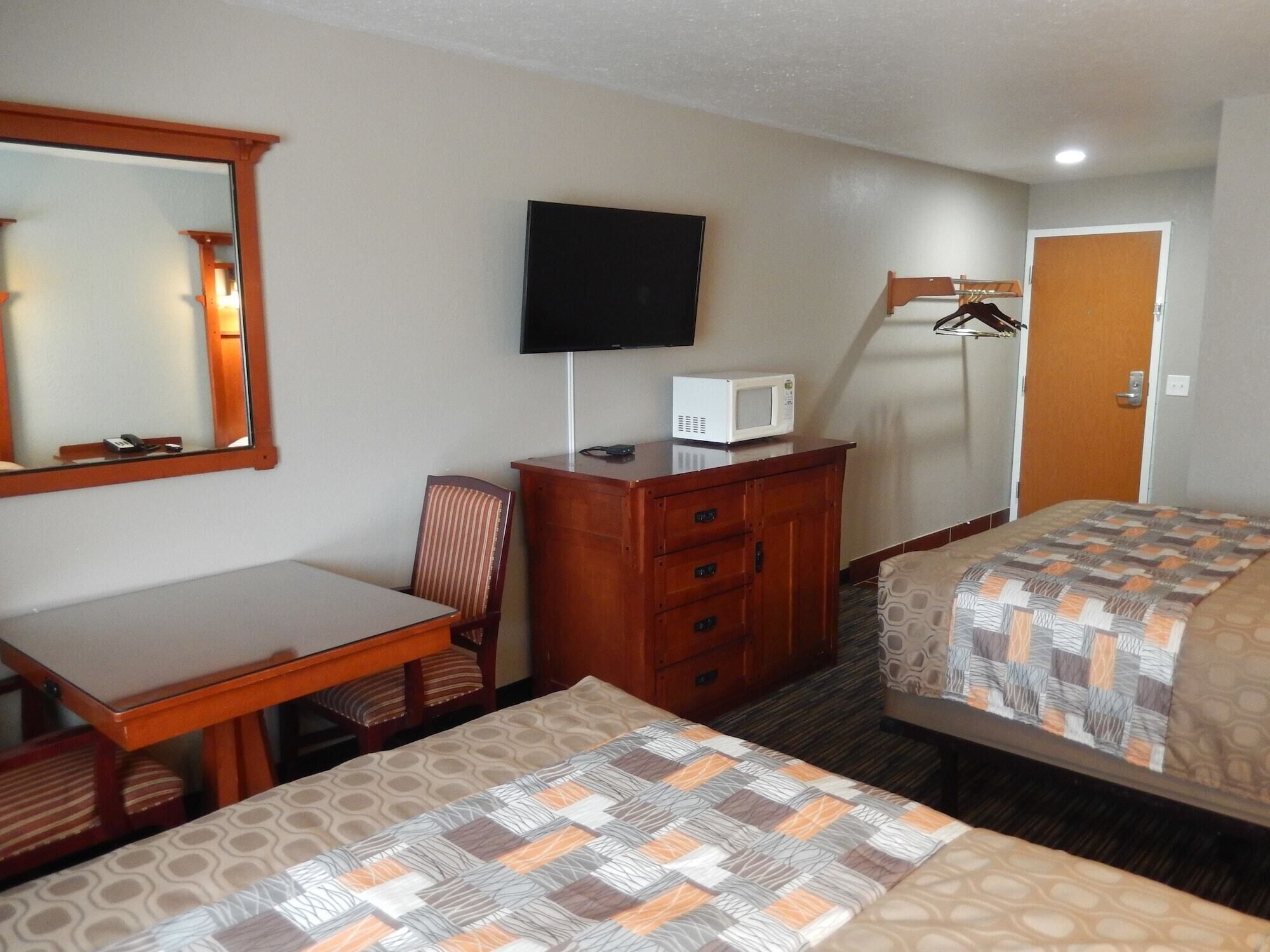 Une chambre d’hôtel avec deux lits, un bureau, une chaise, une télévision, un four à micro-ondes et une armoire.
