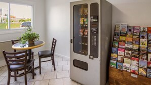 A room with a vending machine, a small table with chairs, a potted plant, and a bulletin board with travel brochures. - Motel 6 Rossford, OH (Rossford)