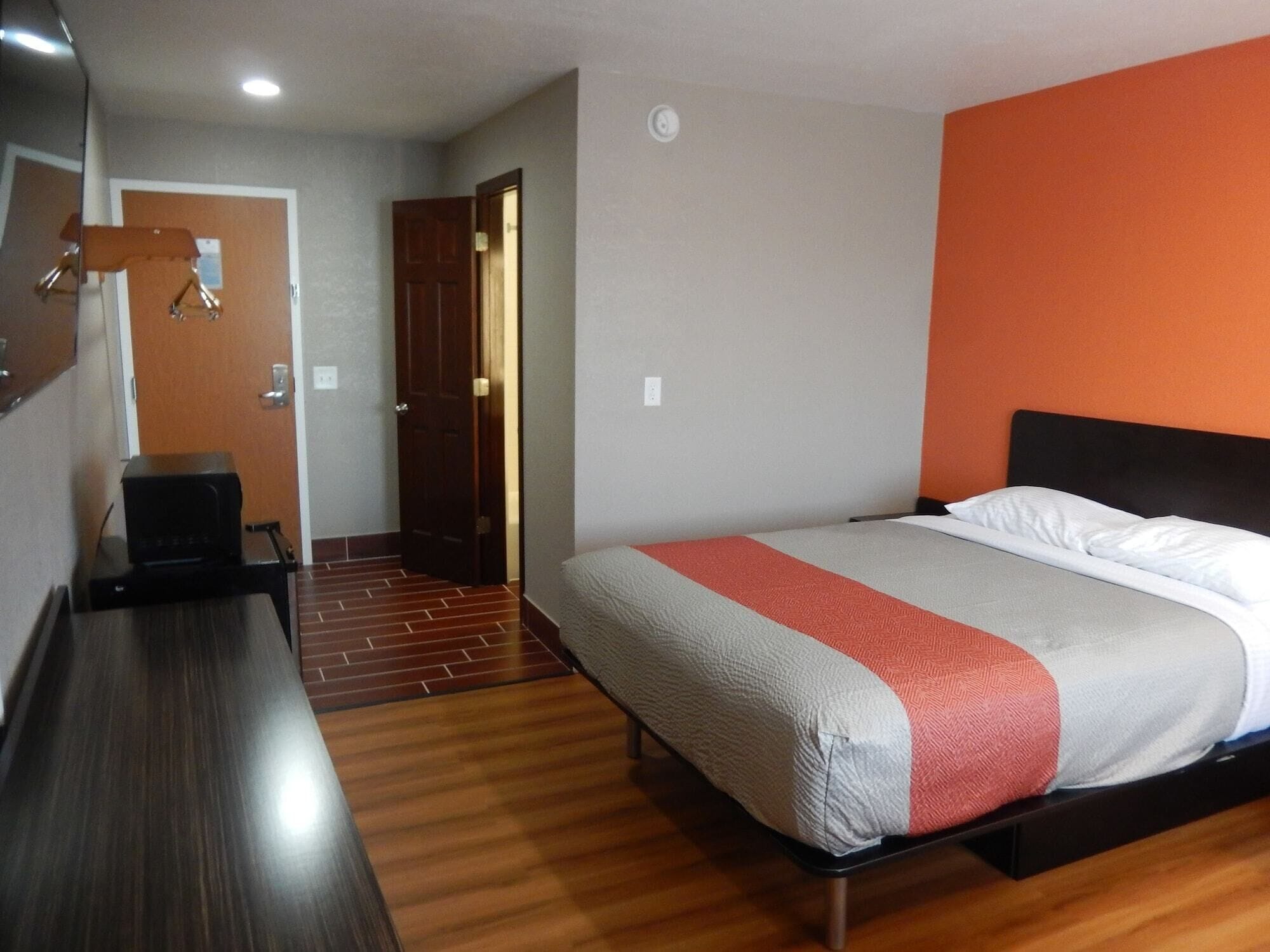A hotel room with a bed, a desk, and a door leading to a hallway.