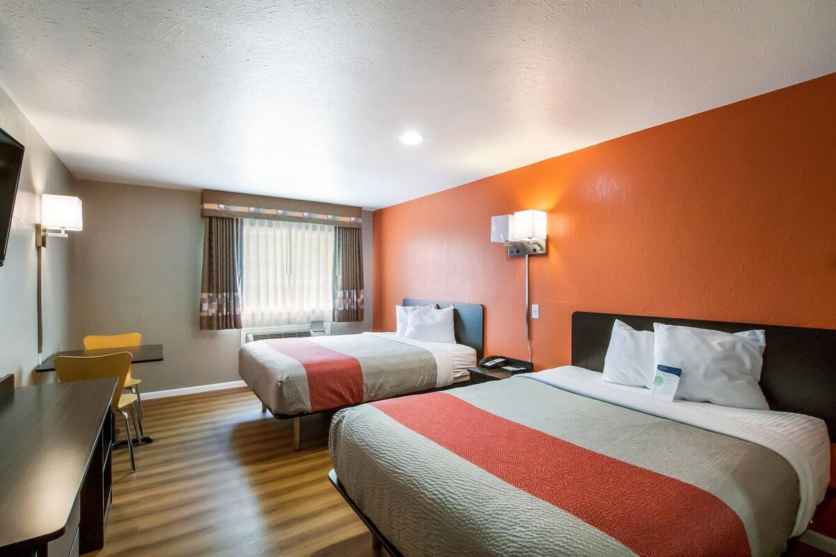 A hotel room with two beds, a desk, and a window with curtains.