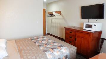 A hotel room with a bed, a wooden dresser, a microwave, and a TV on the wall.
