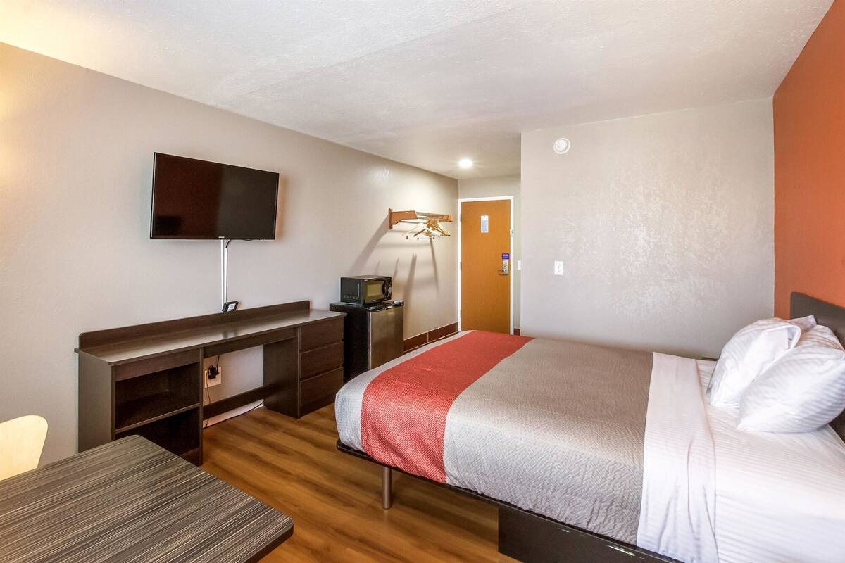 A hotel room with a bed, a desk, a television, a microwave, and a door.