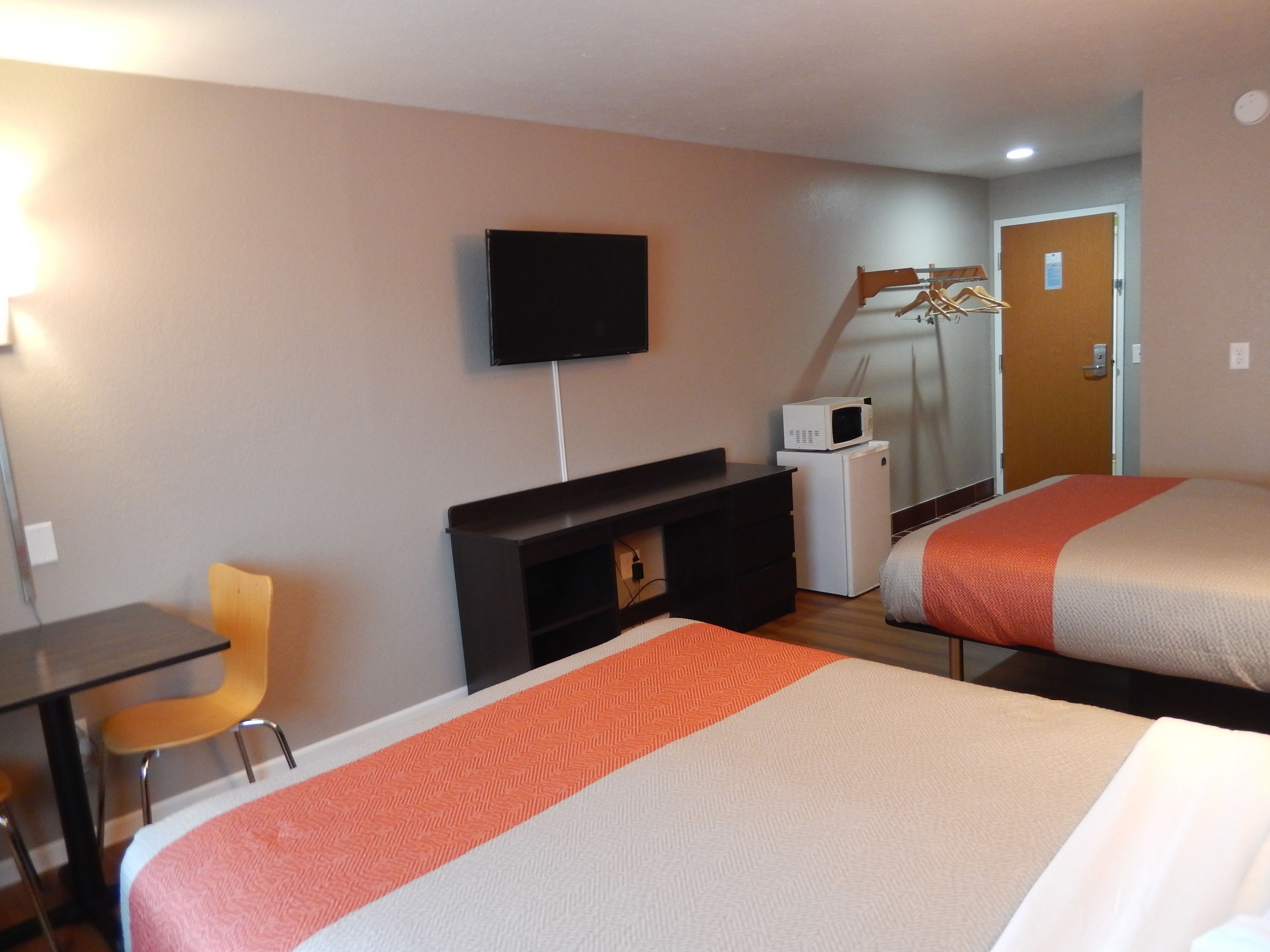 A hotel room with two beds, a desk, a chair, a TV, and a microwave.