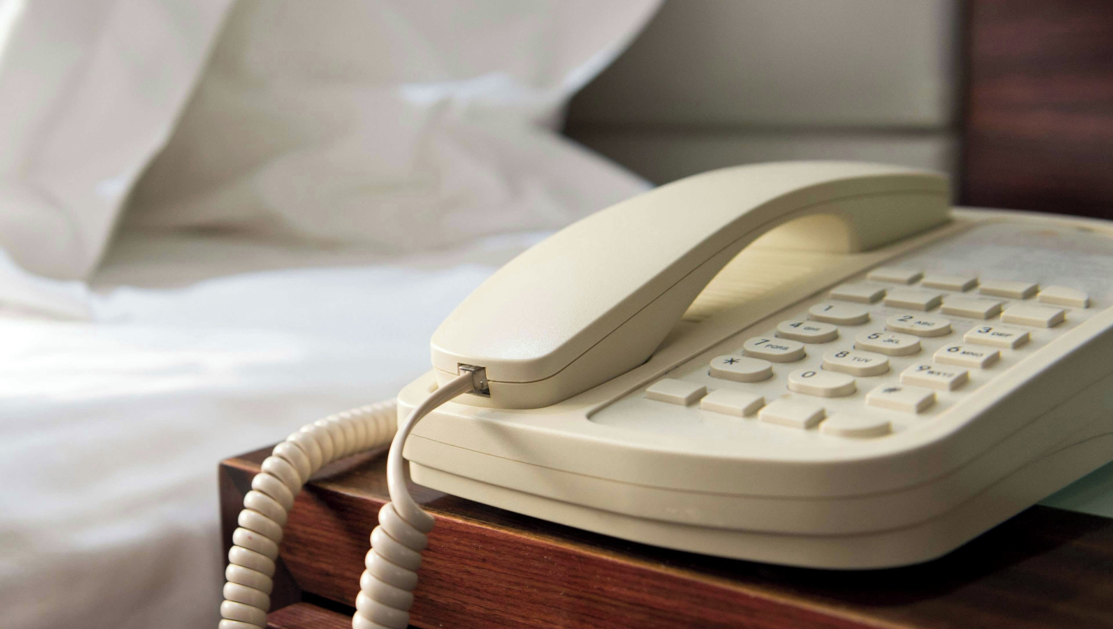 A beige telephone on a wooden bedside table.