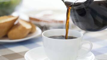 A cup of coffee being poured from a black coffee pot.
