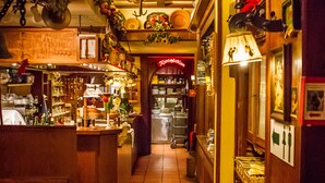 A narrow corridor with wooden walls, tiled flooring, and hanging decorations. There are various items displayed on shelves and counters, and a counter with chairs in the foreground. - Hotel & Restaurant Hackteufel (Heidelberg)
