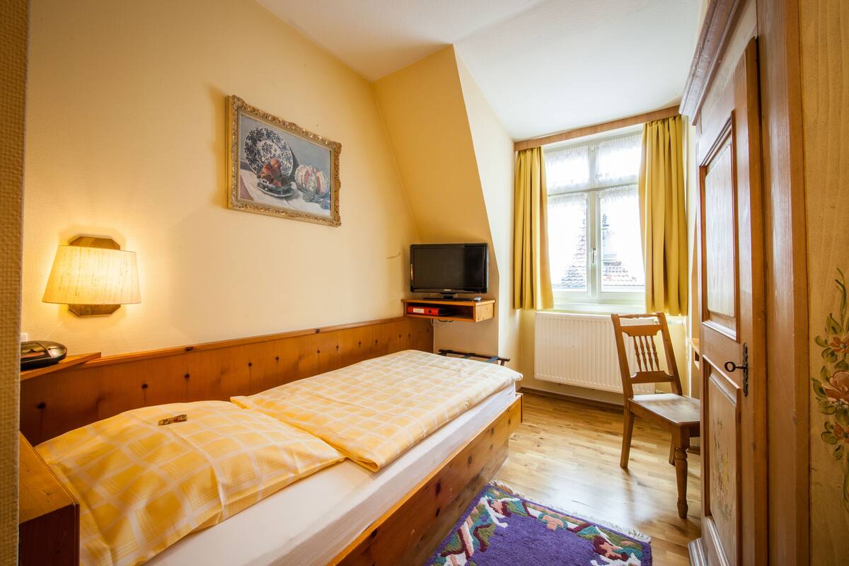 A hotel room with a bed, a television, a chair, and a window with curtains.