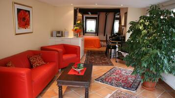 Una sala de estar con un sofá rojo, una mesa de centro con un florero y una planta grande en maceta.
