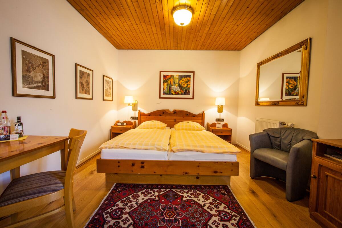 A bedroom with a wooden bed, two bedside tables with lamps, a chair, a sofa, and a large mirror.