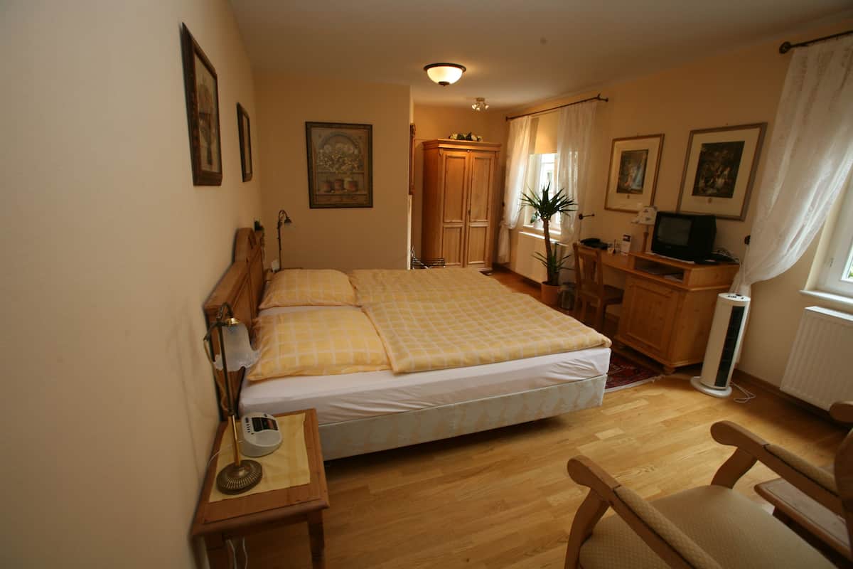 A hotel room with a bed, a desk with a lamp, a chair, a television, and a wardrobe.