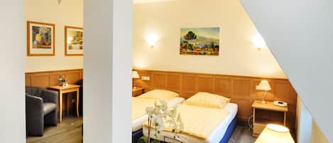 A hotel room with a bed, bedside table, lamp, desk, chair, and a small table with a plant.
