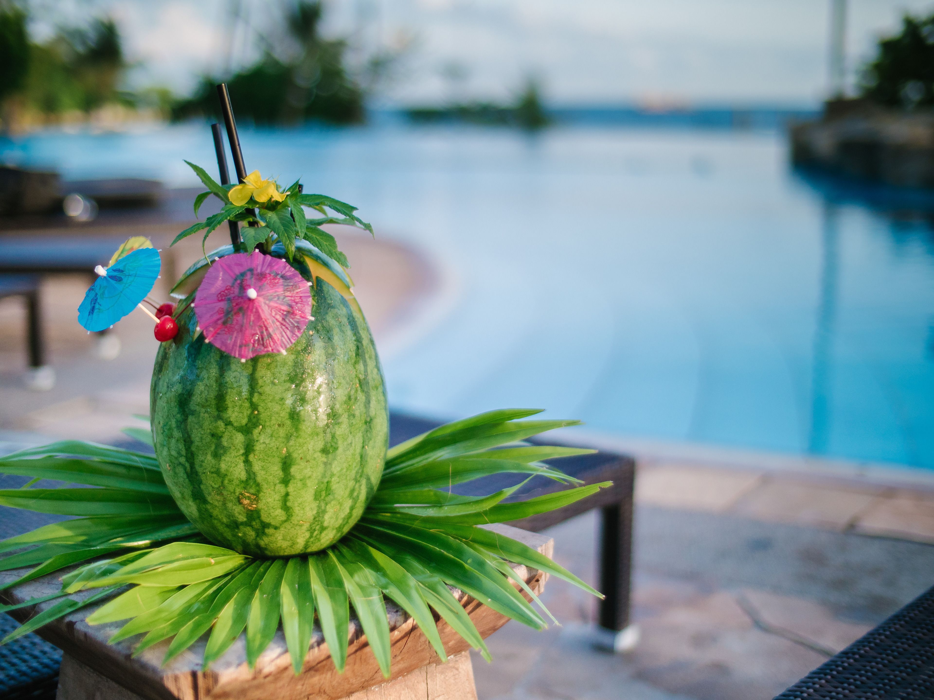 A watermelon with a pink umbrella and a yellow flower on top, placed on a table with green leaves.