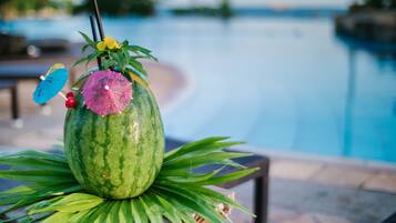 A watermelon with a pink umbrella and a yellow flower on top, placed on a table with green leaves.