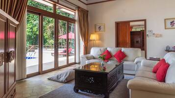 A spacious living room with a white sofa, red cushions, a glass coffee table, and a view of an outdoor pool area.