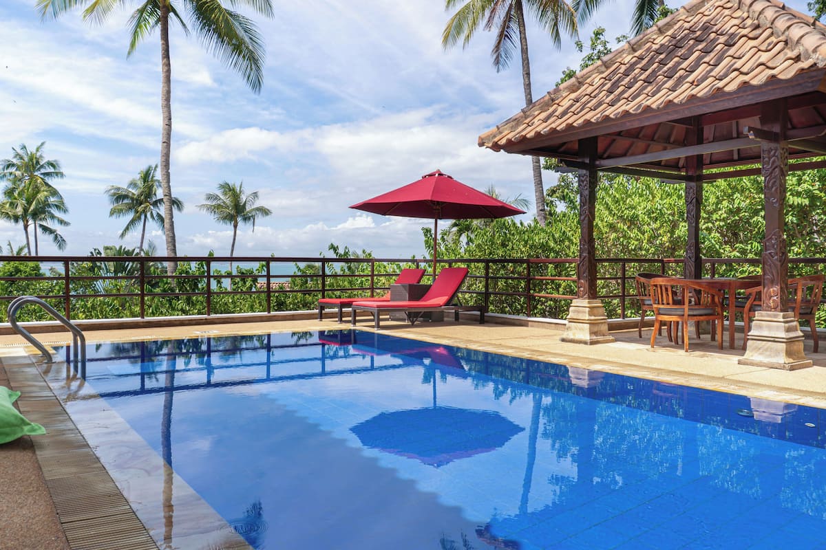 A swimming pool with lounge chairs, a gazebo, and a view of palm trees.