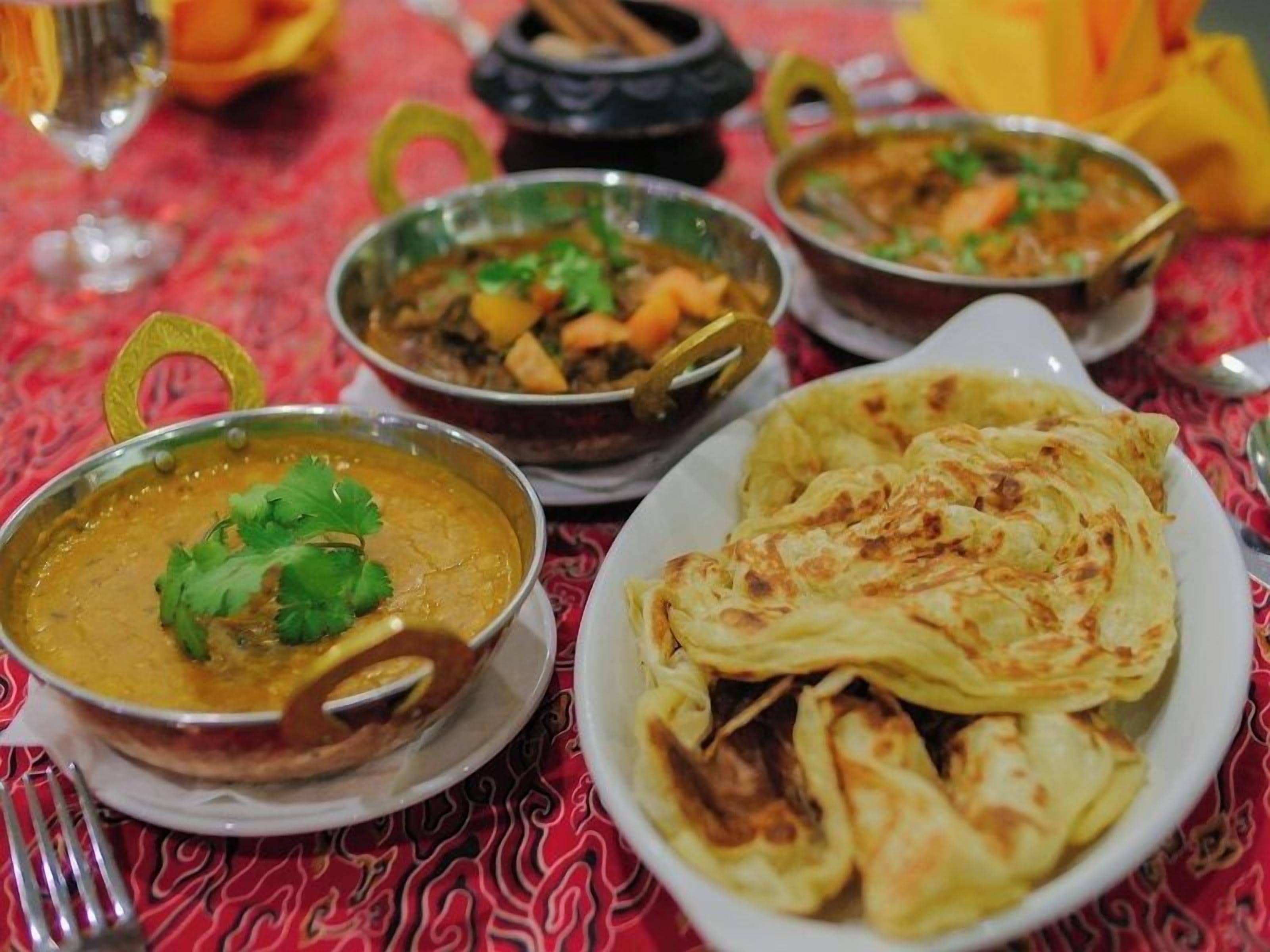 Une table garnie de différents plats, dont un bol de curry et des galettes.