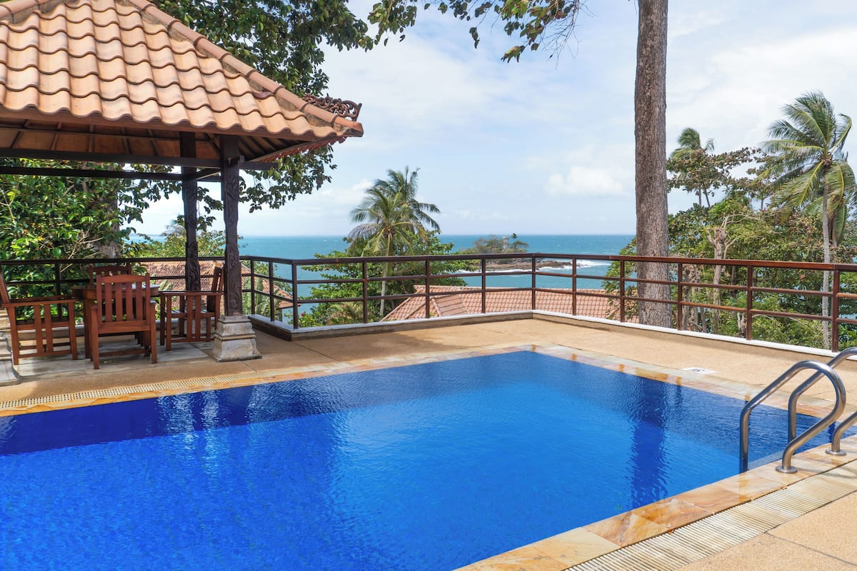 A swimming pool with a view of the ocean, a covered seating area, and a railing.